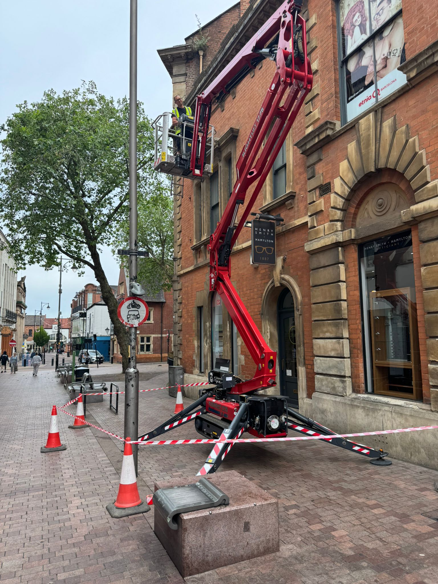 Hinowa Lightlift 17.75 tracked spider lift extended up a town-centre shopfront on Hotel Street, Leicester, with the operative working safely at height